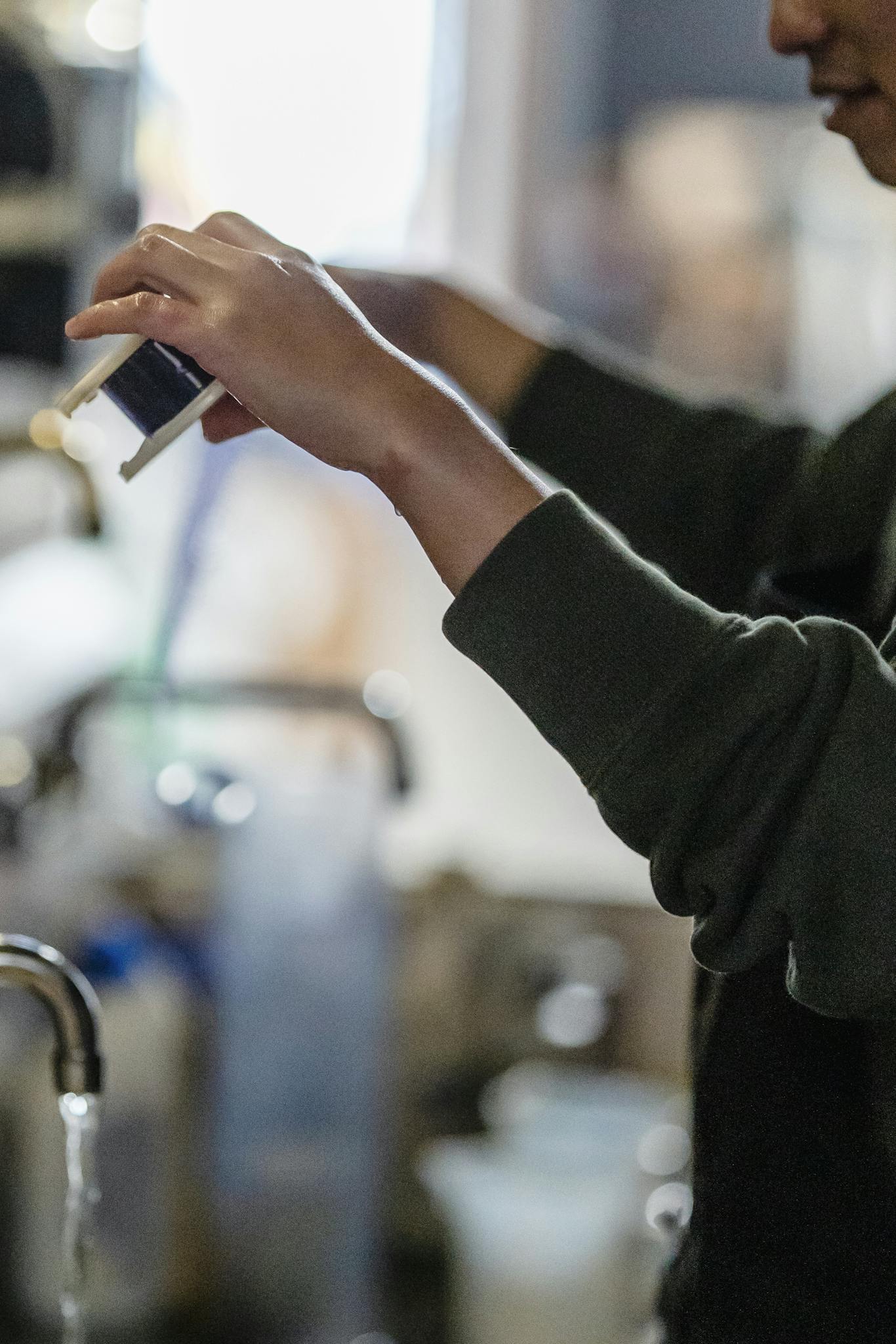 Nahaufnahme von Händen bei der Filmentwicklung in der Dunkelkammer, während fotografische Abzüge im analogen Entwicklungsprozess entstehen.