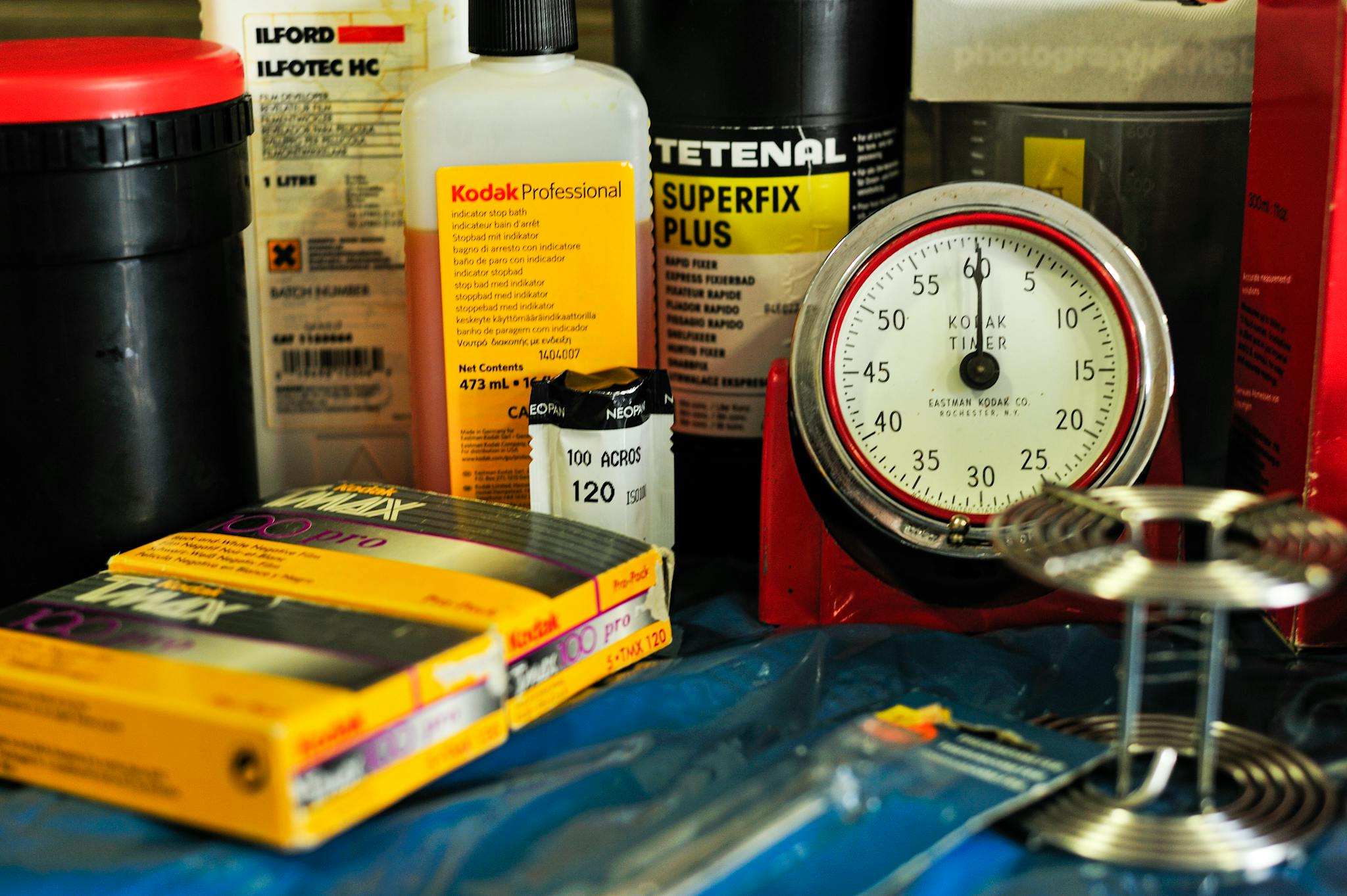 Sammlung analoger Fotografie-Utensilien mit Filmrollen, Entwicklerchemie und einem klassischen Kodak-Timer für die präzise Arbeit in der Dunkelkammer.